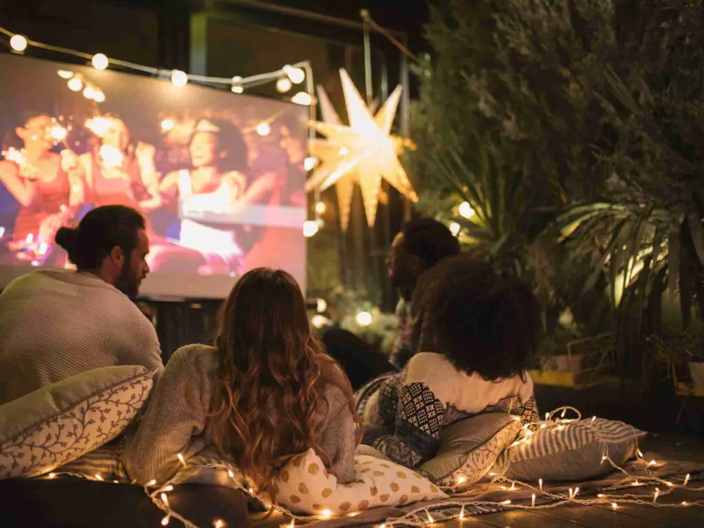 a movie shown on a projector with people sitting in the open and watching it to show outdoor movie nights as a fundraising idea for raising funds for church camps