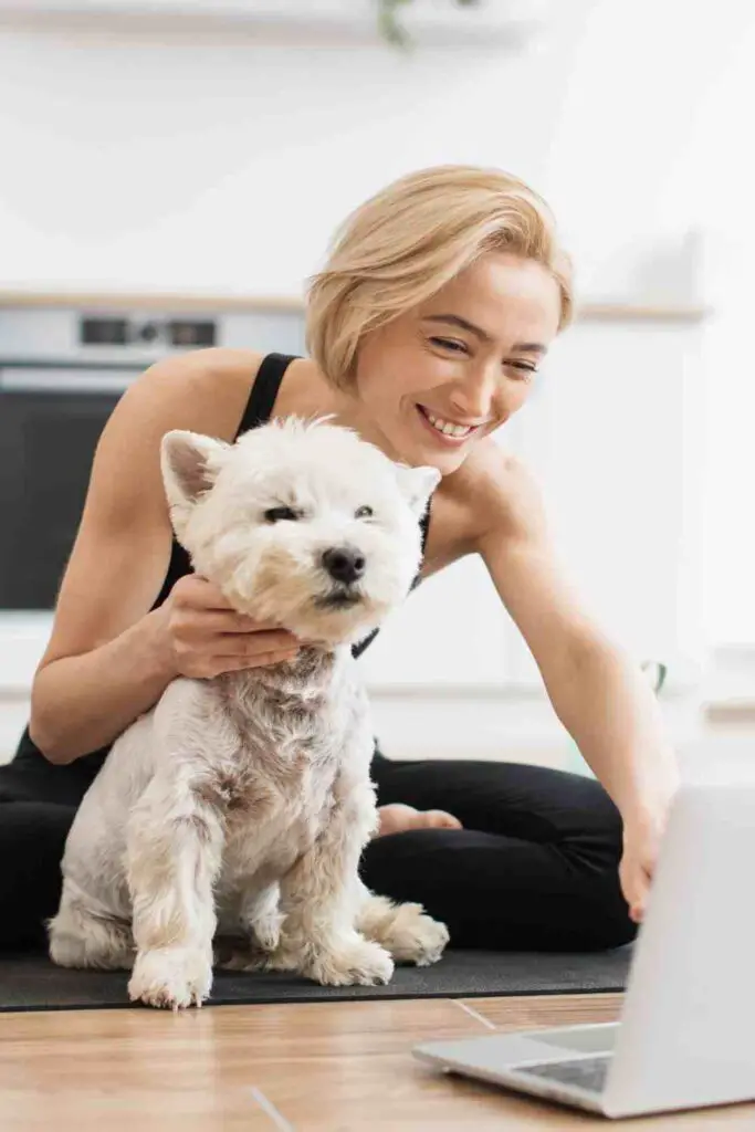 A woman practicing yoga at home with a small dog, likely indicating a pet yoga session.
