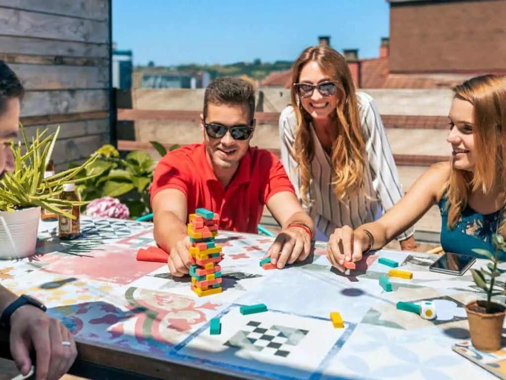 4 friends, 2 male 2 female playing Jenga in backyard during summer